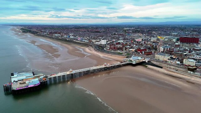 High-altitude drone footage capturing Blackpool's North Pier jutting into the Irish Sea alongside the vast beach and town