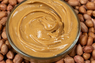 Peanut butter in a bowl among scattered peanuts