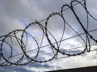 Close-up of barbed wire coils against a cloudy sky. Symbol of security, restriction, or danger....