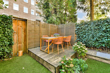 A charming garden dining space featuring a wooden table surrounded by stylish chairs, nestled among lush greenery and wooden fencing.