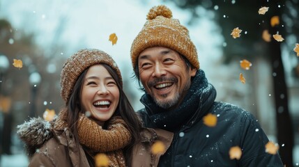 This enchanting winter scene captures a happy couple joyfully embracing the snowy surroundings while leaves fall around them, conveying warmth and love in the cold season.