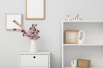 Dresser with shelving unit, different decor and vase of pink blooming branches near white wall in living room