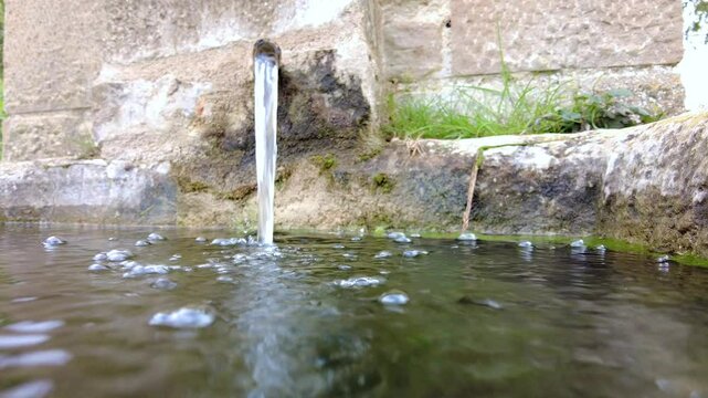 Fresh water flowing from a metal pipe into a stone basin