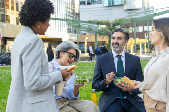 Business people eating lunch together outdoors in city park
