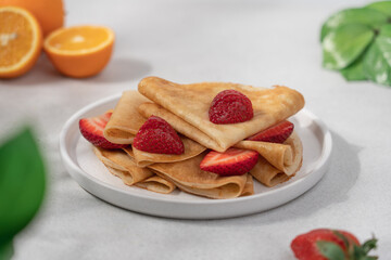 Thin crepes with strawberries in plate on light background. Morning breakfast concept