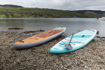 Two paddle boards are moored on the gravel edge of Coniston Water in the Lake District National Park. A long exposure has smoothed the ripples on the water.