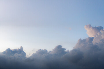 A layer of soft, greyish-blue clouds sits low against a pale, hazy sky. Sunlight gently illuminates the tops, creating subtle highlights.