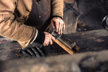 Caucasian blacksmith sharpens knife blade on whetstone, sharpening stone at traditional trade...