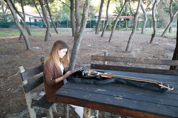 Girl Writes Music Notes On Sheet Music Sitting At The Park Table In The Nature