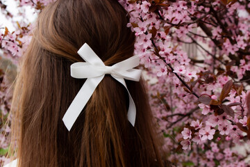Women's hair with a white bow hairpin, against the background of a blossoming tree with pink flowers