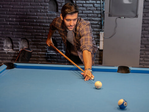 A focused young man lining up a pool shot in a modern bar. 