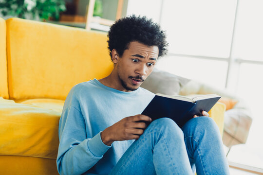 Young man reading an intriguing book while relaxing on a comfortable sofa in a sunny apartment interior