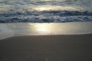 Refletion of the sunlight on the wet beach with wave in background
