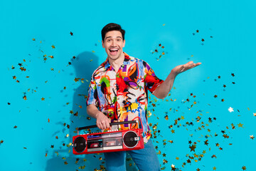 Cheerful young man with colorful shirt holding retro radio and making a joyful gesture surrounded by golden stars