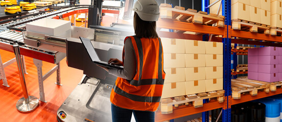 Warehouse automation. Woman engineer developing warehouse tech. Conveyor line in storage area of factory. Warehouse racks. Automation storage area. Woman in orange vest at autonomous enterprise