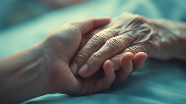 Young hand holding old hand on bed, helping caring for elderly, end of life support, aging people assistance
