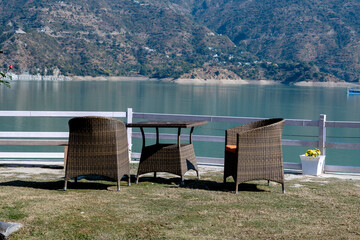 A set of comfy chairs and a table are positioned on the lakeside lawn. This setup encourages visitors to enjoy the beautiful views and fresh air.