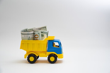 Dollar bills are transported by a yellow and blue toy car on a white background.