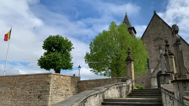 Saint Donat church on a hill at Arlon city centre. Old stone stairs with statues on it leads to the church.  Belgian flag is waving on pole next to the church. Arlon, Belgium
