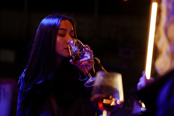 Woman enjoying a drink at a dimly lit bar during a night out with friends