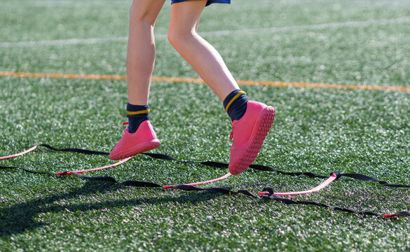 Young athlete performing agility exercises with speed ladder on turf field
