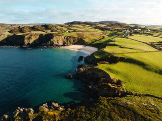 Idyllische Sandbucht umgeben von grünen Hügeln und Klippen in Irland