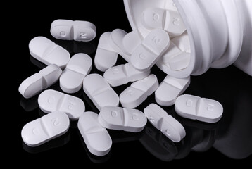 Pills spilling out of a plastic container onto a dark surface