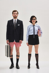 Man and woman in surreal office scene posing with serious faces, wearing mismatched business attire...