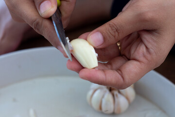 Close-up of hands peeling fresh garlic clove with a knife for cooking preparation