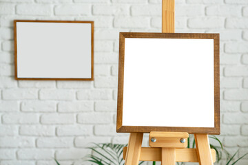 Blank canvas on wooden easel in modern art studio with white brick walls and minimalistic decor