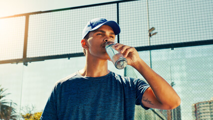 Sports, drinking water and man on tennis court rest for hydration, thirst and wellness outdoors....