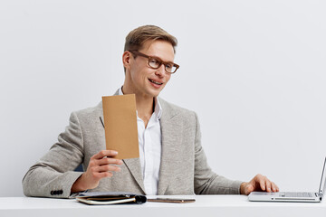 smiling man working with laptop holding brown card wearing glasses grey jacket white shirt isolated...