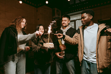 Friends celebrate birthday with cake and sparklers in cozy indoor setting