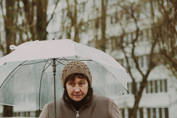 A woman stands outdoors on a rainy day, thoughtfully holding a transparent umbrella. She appears...