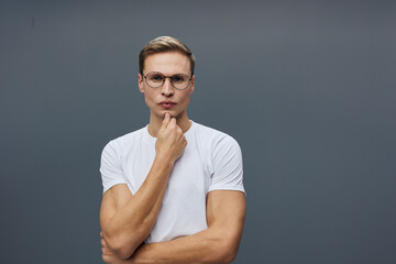 thoughtful young caucasian man wearing glasses white t-shirt look camera hand on chin isolated on...