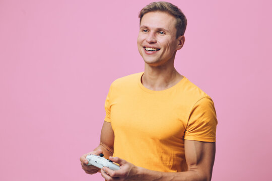 smiling young man holding game controller wear yellow t-shirt look excited play video game isolated pink background cyber security digital wellness concept