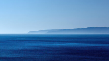 Naklejka premium Serene ocean vista featu deep blue water receding to a hazy distant shoreline under a clear bright sky creating a tranquil and scenic seascape view.