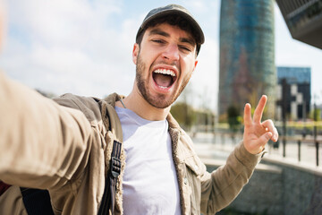 Young man student with backpack and cap taking selfie photo with mobile phone in Barcelona