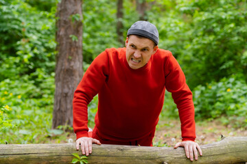 A man performs push-ups using the log as support. The backdrop is a dense forest with trees and foliage.