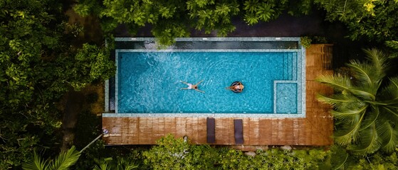 A tranquil moment captured from above, showcasing two individuals relaxing in a beautiful turquoise pool surrounded by lush greenery in Krabi Thailand