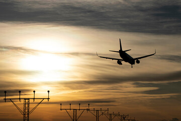 Plane landing, backlit in the sky at a beautiful sunset. A large, beautiful plane. You can see the airport antennas in the background. Clouds in the sky.