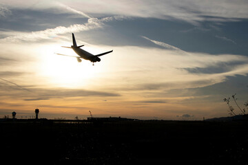 Plane landing, backlit in the sky at a beautiful sunset. A large, beautiful plane. You can see the airport antennas in the background. Clouds in the sky.