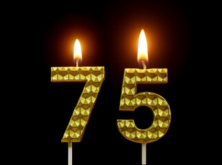 Burning golden birthday candles isolated on black background, number 75.	