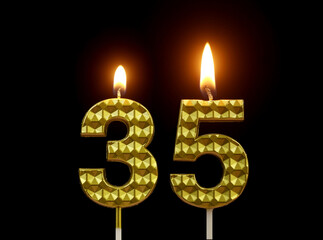 Burning golden birthday candles isolated on black background, number 35.	