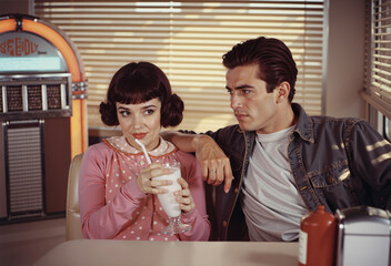 Charming young couple on a date enjoying a milkshake in a retro 1950s diner.