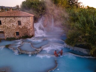 Relaxing in warm, mineral-rich waters at a stunning natural hot spring in SaturniaTuscany Italy. The picturesque landscape, a charming old building and soft steam rising from the turquoise pools.