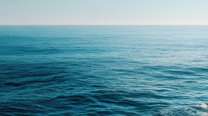 Obraz premium The vast expanse of the calm, clear blue ocean stretches out to the horizon under a cloudless sky, creating a serene and peaceful seascape vista.