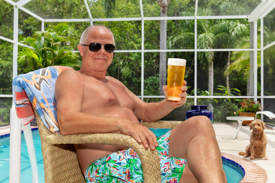 Senior man sitting poolside in his Florida home enjoying a beer.