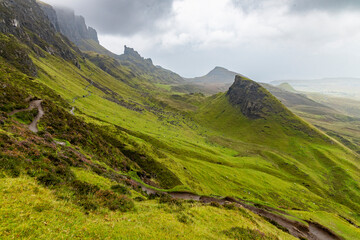 Fototapeta premium The Quiraing, Isle of Skye lush green landscapes, pure air, dramatic cliffs. A surreal trail through wild nature, perfect for trekking, silence, breathing untouched beauty, mystical rock formations.