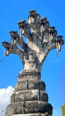 A tall statue featuring a seated figure surrounded by multiple serpent heads against a bright blue...
